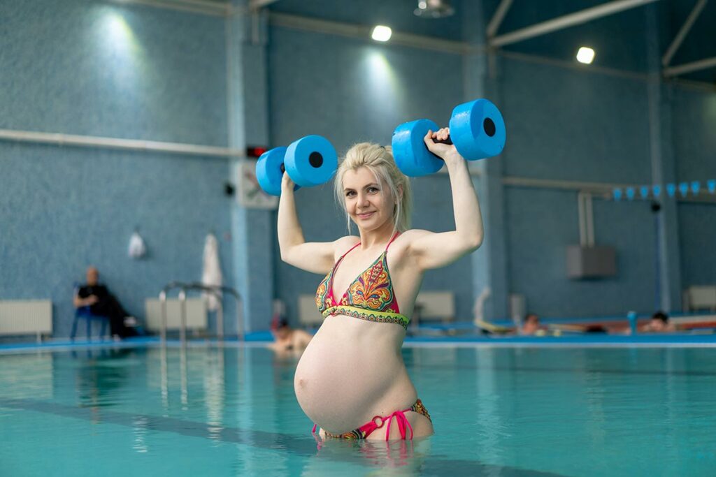 Mulher grávida realizando exercícios na piscina com halteres.